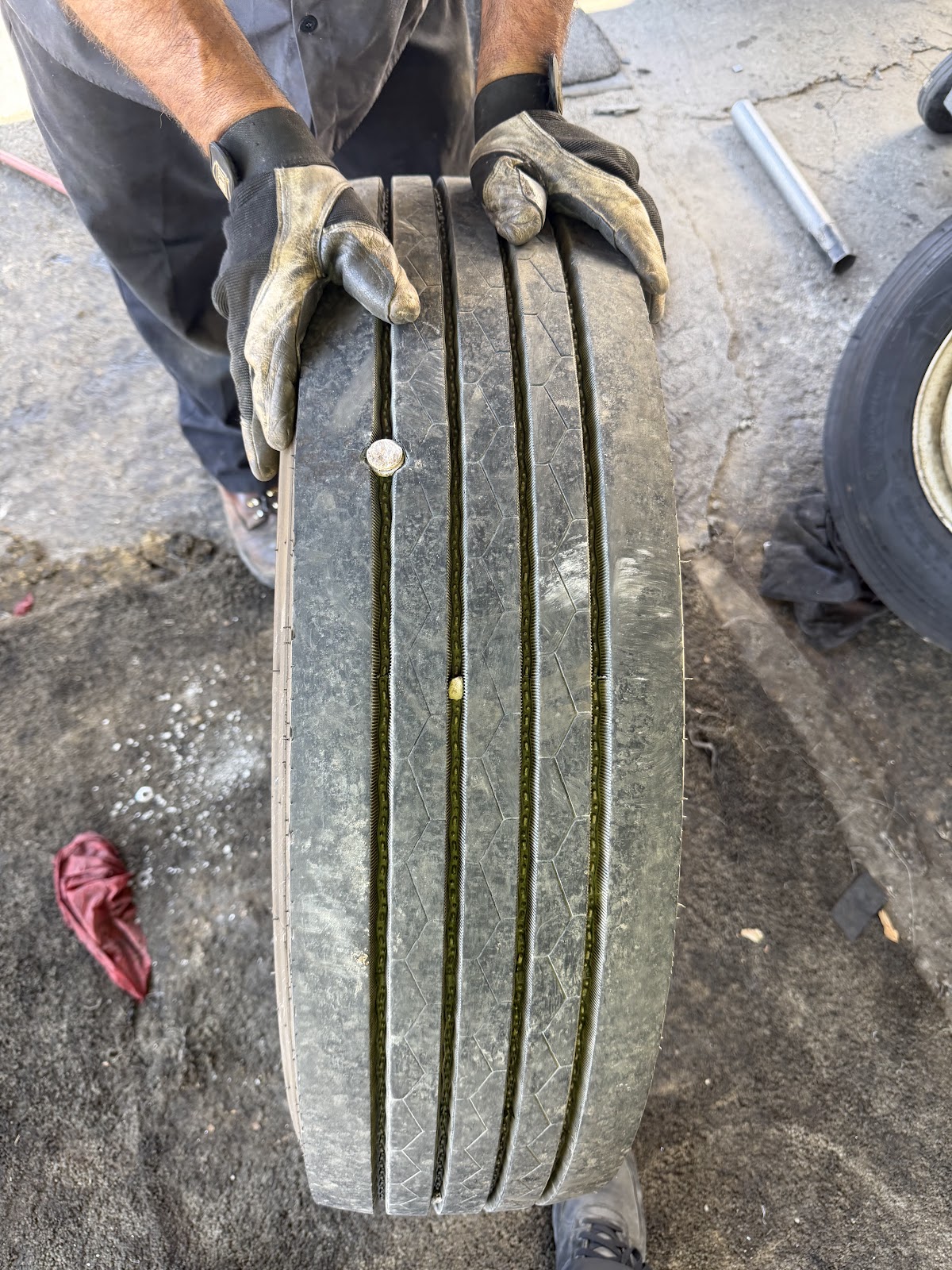 A technician holding a truck tire with nails visibly embedded in the tread