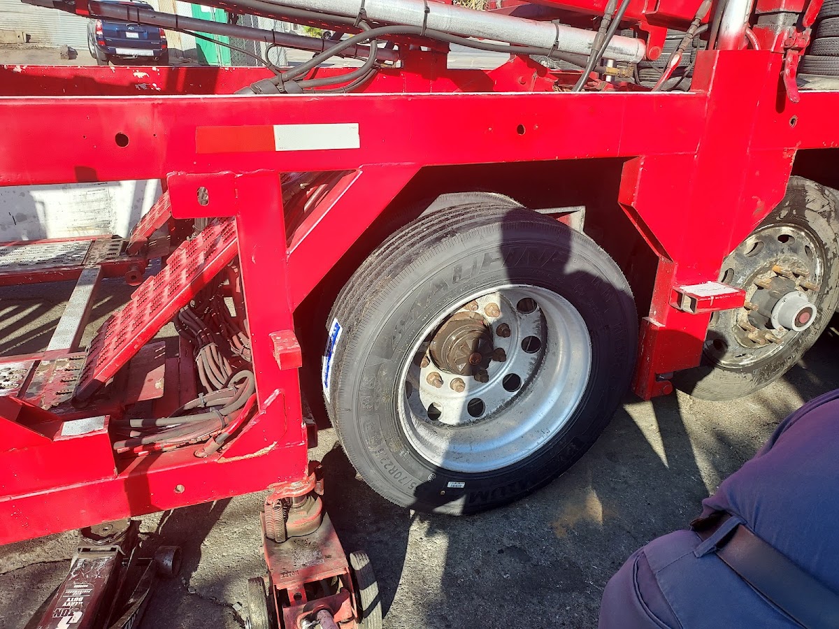 A truck wheel being fitted to a red flatbed trailer in the yard